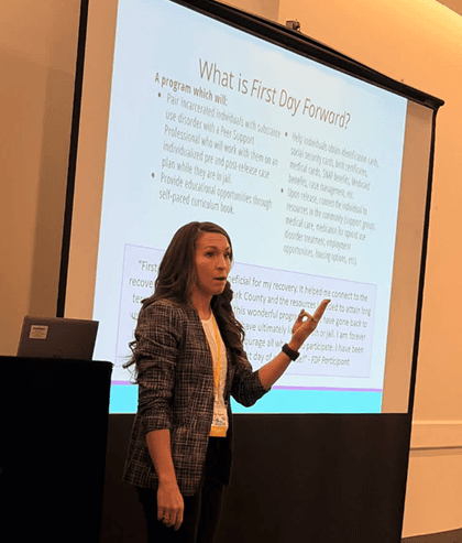 a woman speaking in front of a projector screen a woman speaking in front of a projector screen
