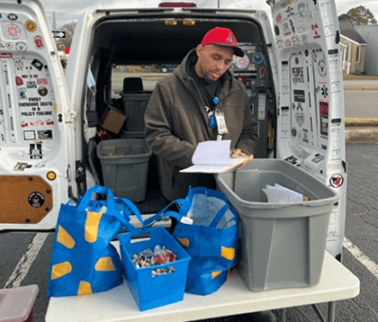 a man in front of an open van trunk behind a table of supplies a man in front of an open van trunk behind a table of supplies