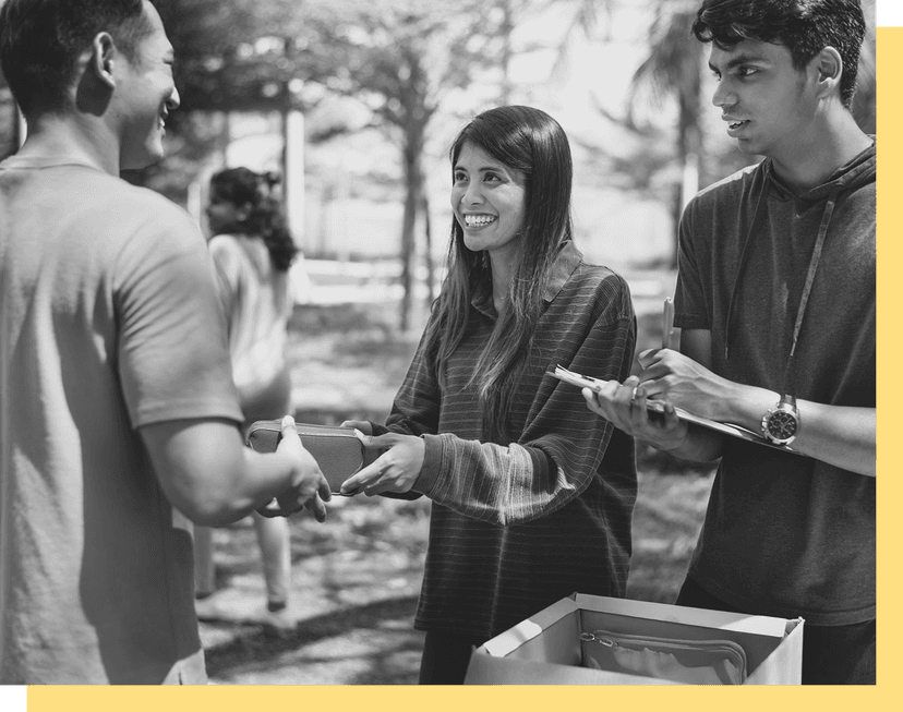 two volunteers smiling as they hand off an item to a smiling man