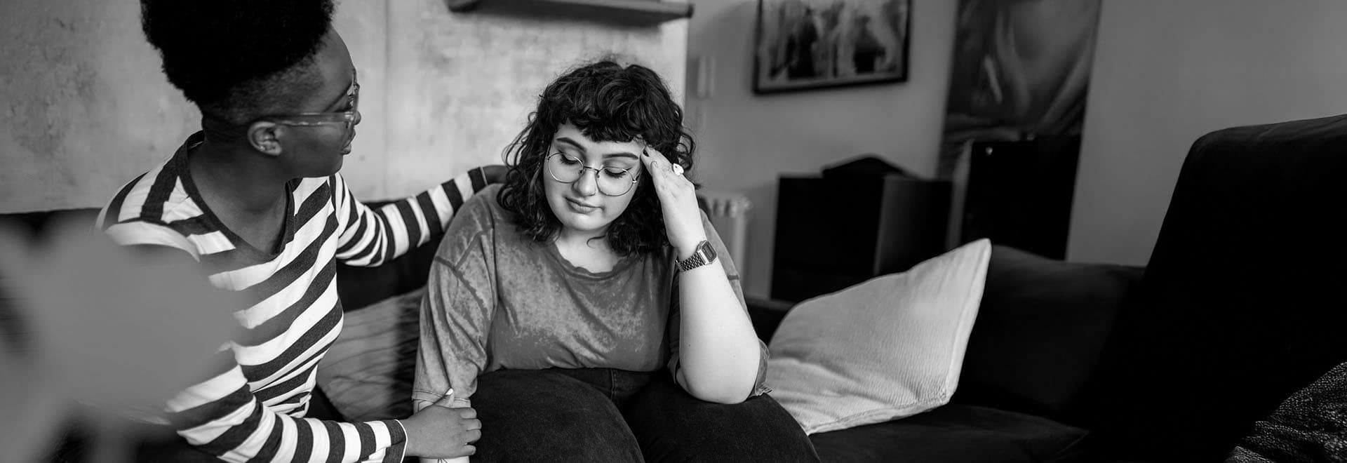 A woman consoling another seemingly distraught woman while sitting on a couch